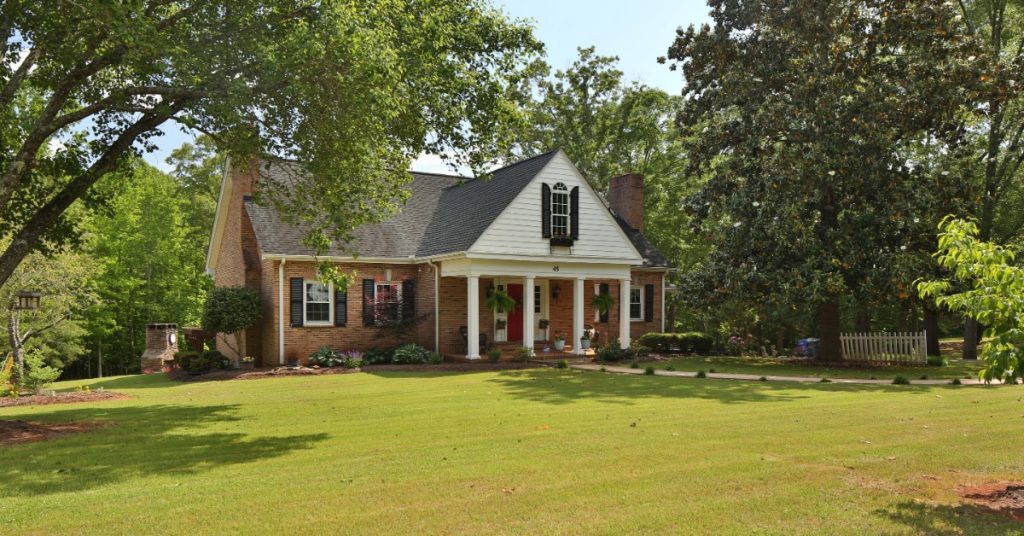 A family home on a lot of acreage. The home is brick with white columns by the front door and trees on the home's sides.