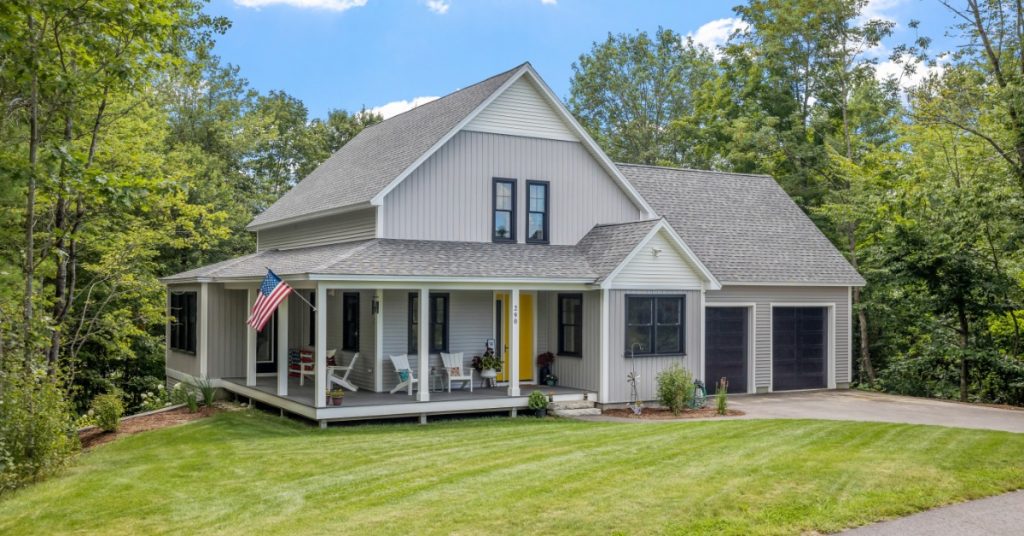 A single-family home with a wrap around front porch and an American flag waving. There are trees on the property.