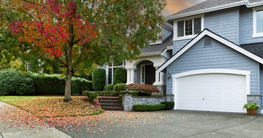 An early autumn day at a blue house with a small tree in the front yard that has leaves in orange and red hues.
